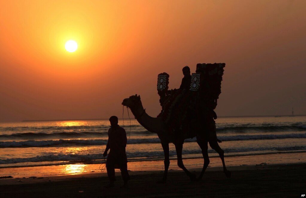 A Pakistani rides a camel on a beach during the last sunset of 2018, in Karachi, Dec. 31, 2018. 