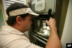 FILE - A home inspector checks air-conditioning coils at a home in the Kendall suburb of Miami.