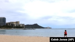 In this April 21, 2020, photo, a woman walks on Waikiki Beach in Honolulu. (AP Photo/Caleb Jones)