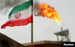 FILE - A gas flare on an oil production platform in the Soroush oil fields is seen alongside an Iranian flag in the Persian Gulf, south of Tehran.