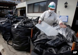 FILE - A worker in a mask collects radioactive trash, placing it in a plastic waste bag at a private house in Minamisoma, Fukushima prefecture, northeastern Japan, Feb. 24, 2016. About 7,000 day laborers are cleaning up this irradiated town.