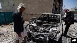 Para pria memperhatikan sebuah mobil yang hancur akibat serangan udara yang dipimpin oleh Arab Saudi di ibukota Yaman, Sana'a, Sabtu, 25 April 2015. (AP Photo/Hani Mohammed)