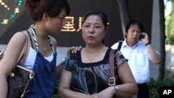 FILE - Xue Min, center, waits with daughter Guo Jie for sentencing at the trial of Xue's brother, Xue Feng, outside Beijing's No. 1 Intermediate People's Court, July 5, 2010. At right is Xue Feng's lawyer, Tong Wei.