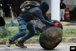 A masked protester rolls a rock onto an avenue after a May Day march turned violent, in San Juan, Puerto Rico, May 1, 2018.