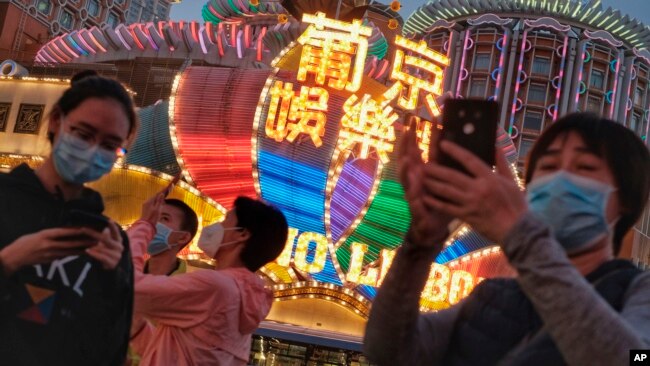 In this Jan, 23, 2020, photo released by Initium Media, tourists wearing masks, take photographs outside the Casino Lisboa in Macao, China. (Choi Chi Chio/Initium Media via AP)