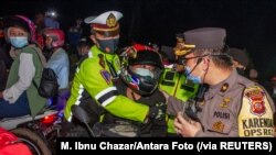 Beberapa polisi mencegat seorang pengendara motor di pos pemeriksaan, di Karawang, Jawa Barat di tengah penerapan larangan mudik menjelang Idulfitri untuk mencegah lonjakan kasus COVID-19, Senin, 10 Mei 2021. (Foto: M. Ibnu Chazar/Antara Foto via Reuters)
