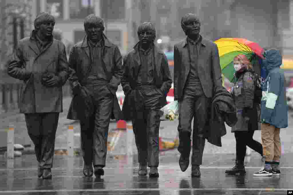 Members of the public wearing face masks stand near a statue of The Beatles in Liverpool, England, as Prime Minister Boris Johnson prepares to lay out a new three-tier alert system for England.