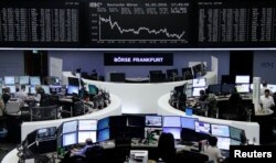FILE - Traders work at their desks in front of the German share price index, DAX board, at the stock exchange in Frankfurt, Germany, Feb. 16, 2016.