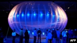FILE - Visitors stand next to a high altitude WiFi internet hub, a Google Project Loon balloon, on display at the Air Force Museum in Christchurch.