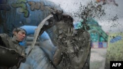 FILE - A reveller throws a bucket of mud during the 17th Boryeong mud festival at Daecheon beach in Boryeong, 150 kilometers southwest of Seoul, on July 18, 2014. The annual festival aims to promote the use of the mineral-rich mud for cosmetic skin-care. (AFP PHOTO / Ed Jones)