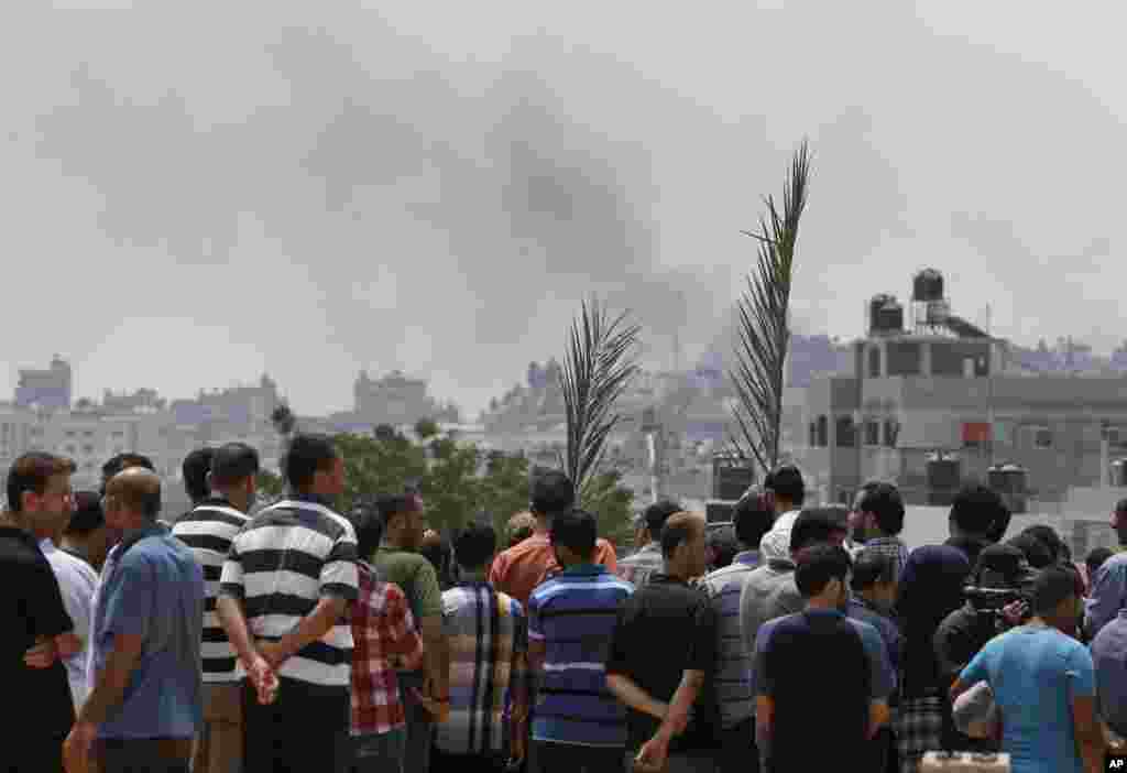 As smoke rises in the skyline from an Israeli strike, mourners holding palm tree fronds gather to bury seven members of the Kelani family killed overnight by an Israeli strike in Gaza City, in Beit Lahiya, northern Gaza Strip, July 22, 2014.