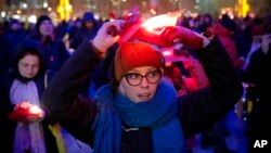 A woman holds a red paper as people display Romania's red, yellow and blue flag during an anti-government protest in Bucharest, Romania, Dec. 1, 2018, as Romanians celebrate 100 years since the country became a modern-day state.