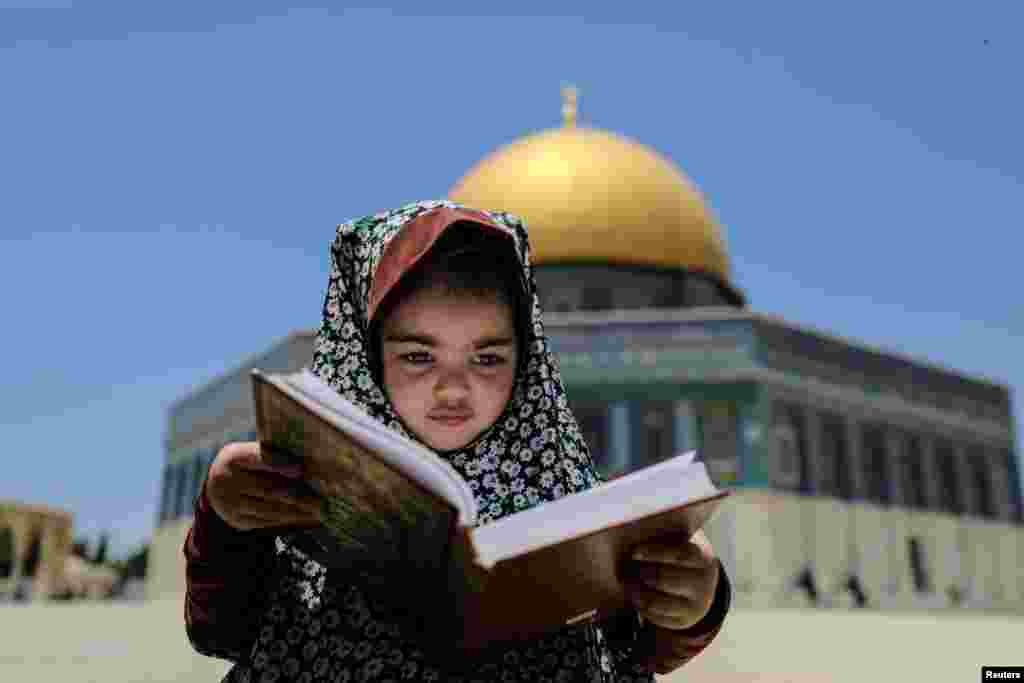 A girl sits with a holy book as the Dome of the Rock is seen in the background at the compound that houses al-Aqsa Mosque, known to Muslims as Noble Sanctuary and to Jews as Temple Mount, in Jerusalem&#39;s Old City.