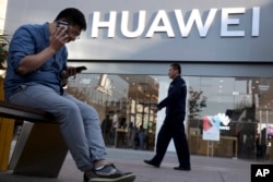 Seorang pria menggunakan dua ponsel pintar sekaligus di depan toko Huawei di Beijing, 20 Mei 2019.