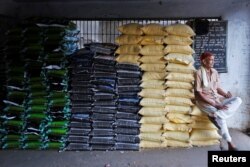 FILE - A laborer sits on sacks of food grains while waiting for customers at a wholesale market in Ahmedabad, India, Dec. 14, 2016.