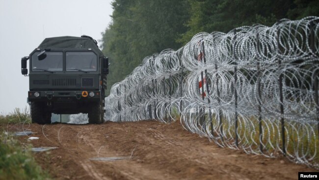 FILE - A vehicle drives next to a fence built by Polish soldiers on the border between Poland and Belarus near the village of Nomiki, Poland, August 26, 2021.