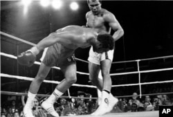 FILE - An Oct. 30, 1974 file photo shows Challenger Muhammad Ali watching as defending world champion George Foreman goes down to the canvas in the eighth round of their WBA/WBC championship match in Kinshasa, Zaire.