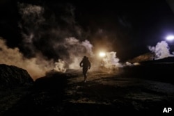 Migrants run as tear gas is thrown by U.S. Border Protection officers to the Mexican side of the border fence after they climbed the fence to get to San Diego, from Tijuana, Mexico, Jan. 1, 2019.