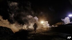 FILE - Migrants run as tear gas is thrown by U.S. Border Protection officers to the Mexican side of the border fence after they climbed the fence to get to San Diego, from Tijuana, Mexico, Jan. 1, 2019. 