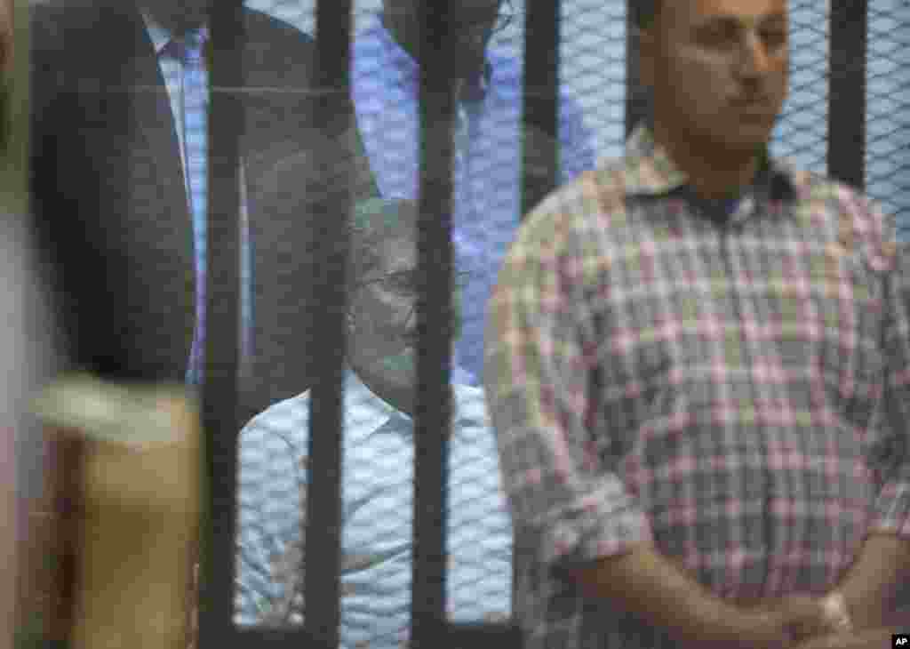 Polisi berpakaian preman menjaga presiden terguling Mohamed Morsi di pengadilan dalam akademi polisi nasional Mesir di Kairo (21/4).