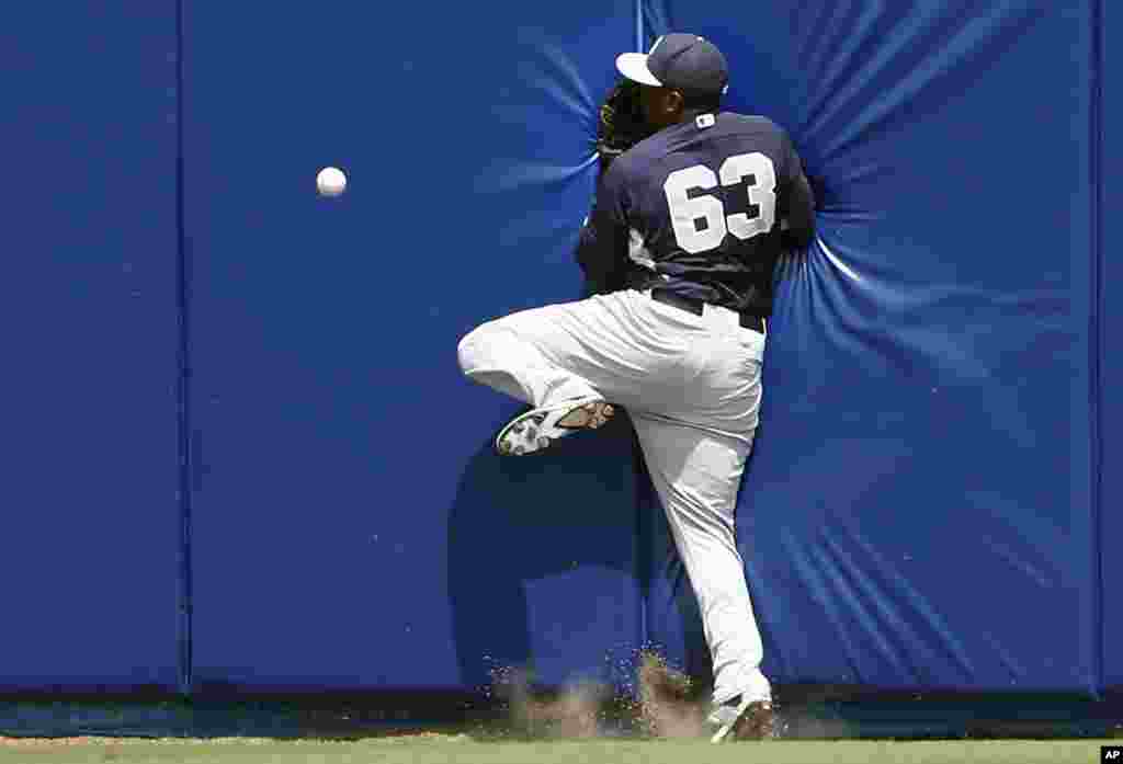 New York Yankees center fielder Jose Pirela crashes into the wall as he chases a ball hit for an inside-the-park home run hit by New York Mets&#39; Juan Lagares in the first inning of a spring training baseball game in Port St. Lucie, Florida.