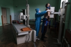 A medic prepares a coronavirus patient for a lung X-ray at a hospital in Stryi, Ukraine, Tuesday, Sept. 29, 2020. (AP Photo/Evgeniy Maloletka)