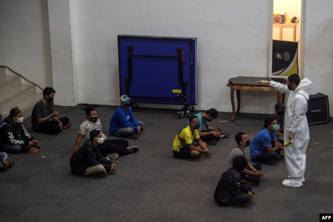 Seorang petugas medis (kanan) dari kepolisian memberi pengarahan kepada sejumlah warga yang melanggar Pembatasan Sosial Berskala Besar (PSBB) di Surabaya, 3 Mei 2020. (Foto: AFP)