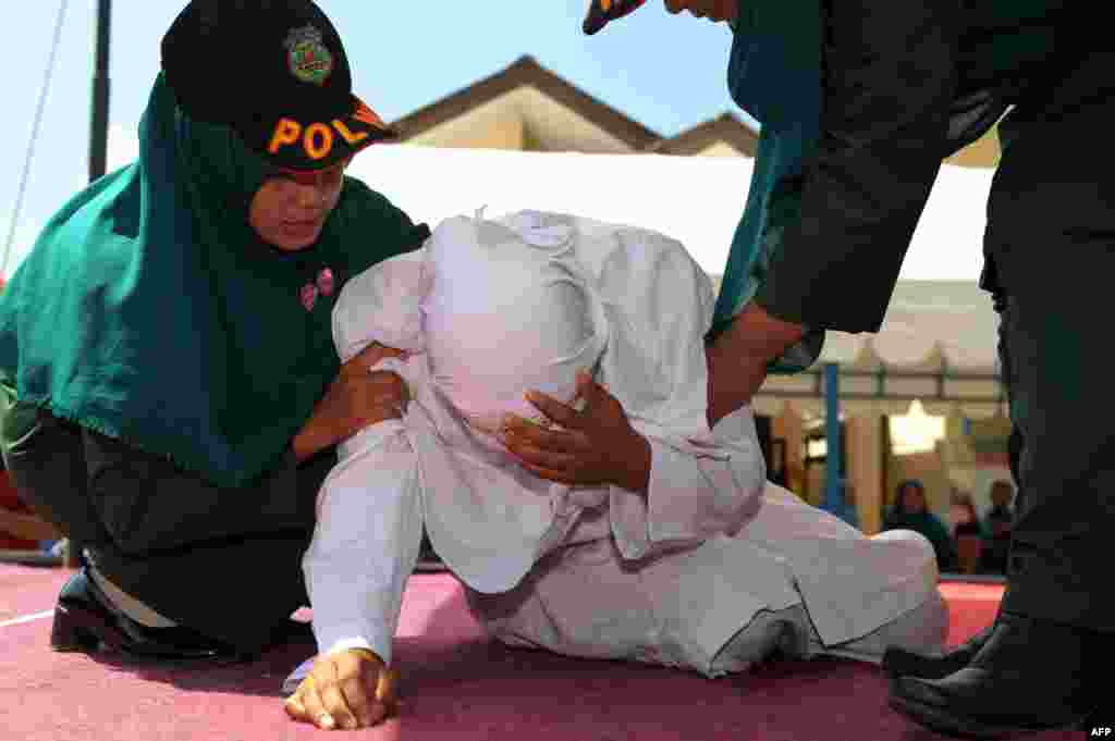 An Indonesian woman known as Linda (C) is helped by two Sharia officials after being caned for spending time in close proximity with a man who is not her husband, which is against Sharia law, in Banda Aceh.