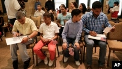 Derek Martinez, second from left, and Jason Victoria, second from right, watch as their fathers, Alex Martinez and Melvin Victoria place their certificates of citizenship in mounting folders after a ceremony at the Bronx Zoo, Tuesday, May 26, 2015, in New York. (AP Photo/Julie Jacobson)