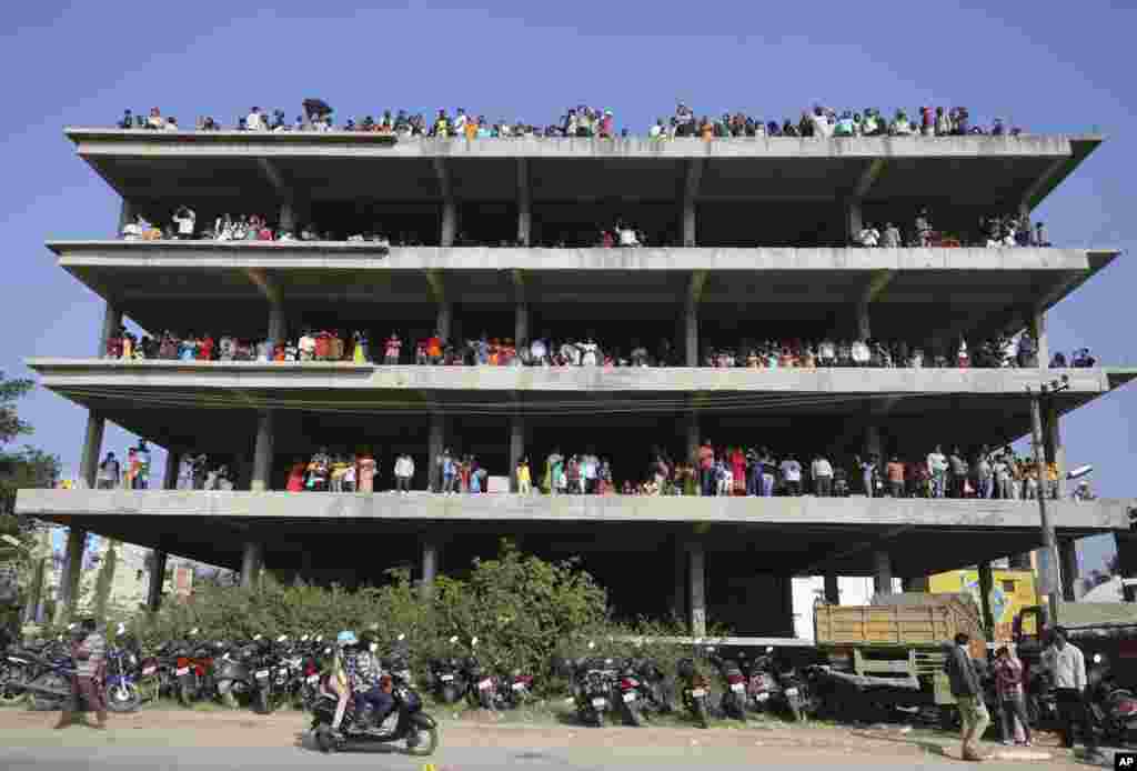 People stand on an under construction building outside Yelahanka air base and watch Indian Air Force Suryakiran aircrafts perform aerobatic maneuvers on the second day of Aero India 2021 in Bengaluru, India.