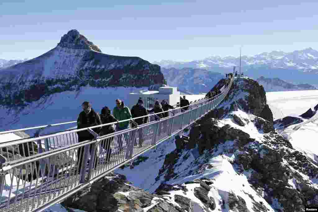 Du khách đi trên cây cầu 'Peak Walk' trong một buổi ra mắt giới truyền thông, ở Glacier 3000 tại Les Diablerets, Thụy Sĩ. Được xây dựng giữa hai đỉnh núi Scex Rouge và View Point ở độ cao 3.000 mét, cây cầu treo dài 107 m và rộng 80 cm là cây cầu đầu tiên trên thế giới nối liền hai đỉnh núi với nhau. 