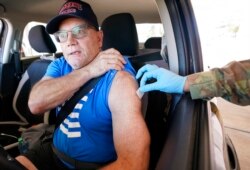 Sitting in his car, Mesquite firefighter Jeffrey Dillon pulls up his shirt sleeve to get a Pfizer COVID-19 vaccine booster shot at the Dallas County Health and Human Services drive up vaccine site in Mesquite, Texas, Nov. 30, 2021.