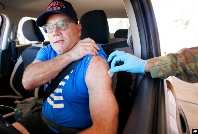 Sitting in his car, Mesquite firefighter Jeffrey Dillon pulls up his shirt sleeve to get a Pfizer COVID-19 vaccine booster shot at the Dallas County Health and Human Services drive up vaccine site in Mesquite, Texas, Nov. 30, 2021.