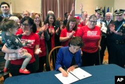 FILE - Cheers erupt as Rhode Island Gov. Gina Raimondo signs an executive order Feb. 26, 2018, in Warwick, R.I., to establish a new policy to try to keep guns away from people who show warning signs of violence.