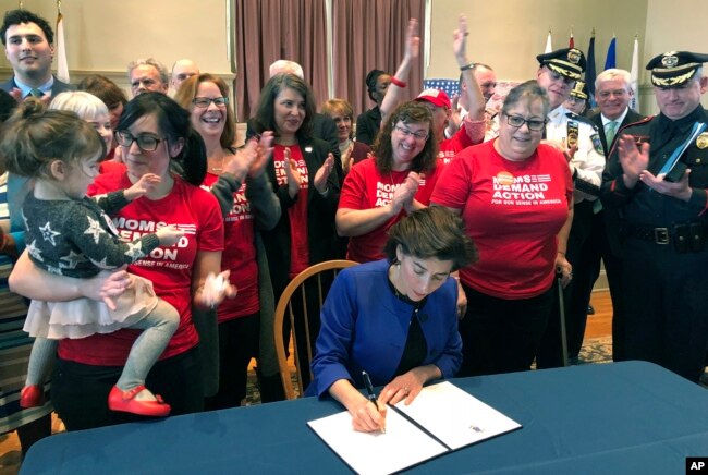 FILE - Cheers erupt as Rhode Island Gov. Gina Raimondo signs an executive order Feb. 26, 2018, in Warwick, R.I., to establish a new policy to try to keep guns away from people who show warning signs of violence.
