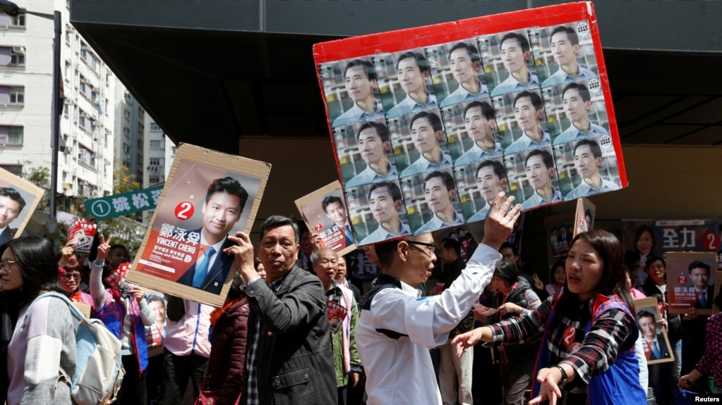 香港立法会补选期间，民主派候选人姚松炎的支持者手举他的画像从手举亲北京的民建联候选人郑泳舜的画像的支持者旁边走过。（2018年3月11日）