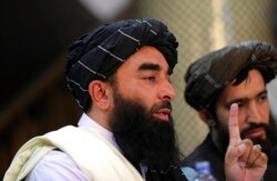 Juru bicara Taliban Zabihullah Mujahid, kiri, berbicara pada konferensi pers pertamanya di Pusat Informasi Media Pemerintah, di Kabul, Afghanistan, Selasa, 17 Agustus 2021. (Foto: AP)