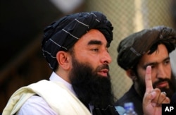 Juru bicara Taliban Zabihullah Mujahid, kiri, berbicara pada konferensi pers pertamanya di Pusat Informasi Media Pemerintah, di Kabul, Afghanistan, Selasa, 17 Agustus 2021. (Foto: AP)