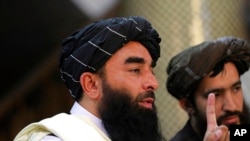 Taliban spokesman Zabihullah Mujahid, left, speaks at his first news conference at the Government Media Information Center, in Kabul, Afghanistan, Tuesday, Aug. 17, 2021. 