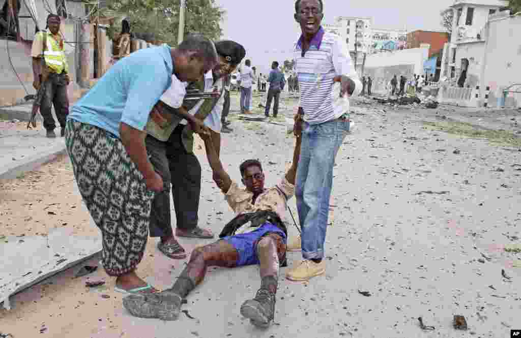 2013年6月19日，摩加迪沙一处联合国大院遭到袭击后，索马里民众和一名警察把一名在袭击中受伤的政府军士兵抬走。