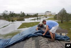 Jeff Pyron, left, and Daniel Lilly cover Lilly's roof after Tropical Storm Florence hit Davis, N.C., Sept. 15, 2018. The town had 4½ feet of storm surge.