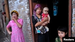 一名维吾尔女子抱着她的儿子站在门口（路透社，2012年7月22日）