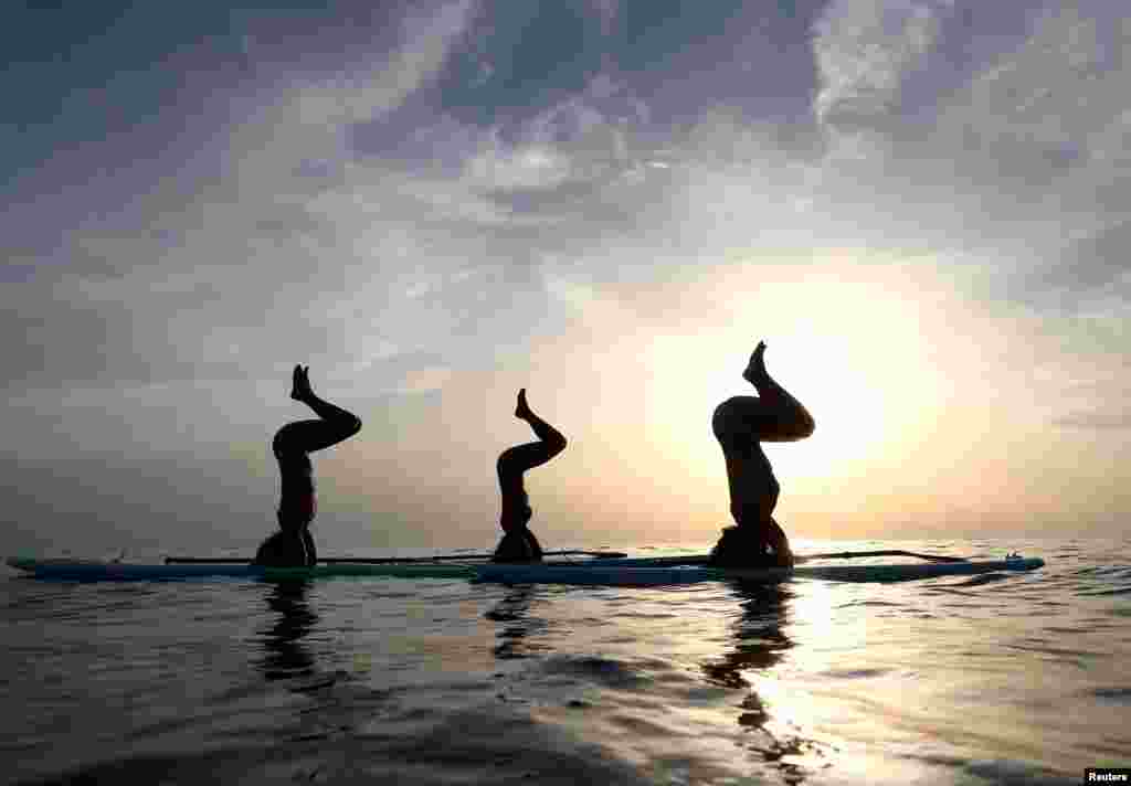 Tiga orang melakukan yoga di atas papan selancar di pantai Adriatik, Verudela, Kroasia.