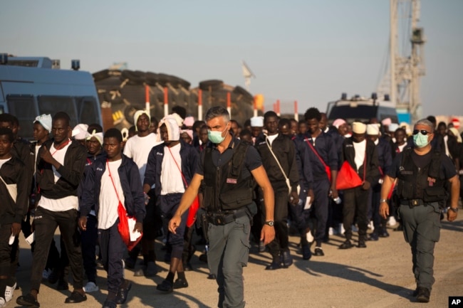 FILE - Italian border police officers escort sub-Saharan men on their way to a relocation center, after arriving aboard the Golfo Azzurro rescue vessel at the port of Augusta, in Sicily, Italy, June 23, 2017.