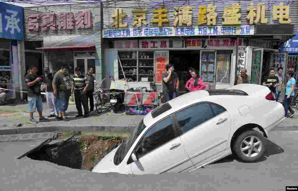 Para pejalan kaki memperhatikan mobil yang terpuruk separuh di lubang di sebuah jalan di Beijing, China, 6 September 2015.