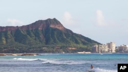 FILE - Surfers ride waves off Ala Moana Beach Park in Honolulu, with Diamond Head mountain in the background. Out of sight of tourists are disused military tunnels beneath the crater.