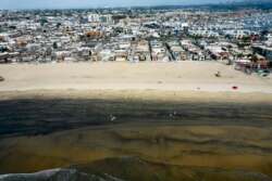 In this aerial image taken with a drone, workers in protective suits clean the contaminated beach after an oil spill in Newport Beach, Calif., on Wednesday, Oct. 6, 2021.
