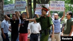 A policeman tries to stop anti-China protesters holding placards during a demonstration in front of the Philippines embassy in Hanoi, Vietnam, July 17, 2016. 