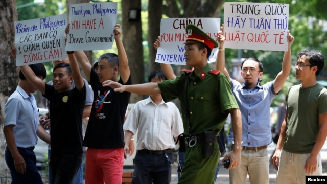 A policeman tries to stop anti-China protesters holding placards during a demonstration in front of the Philippines embassy in Hanoi, Vietnam, July 17, 2016. 