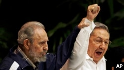 FILE - In this April 19, 2011 photo, Fidel Castro, left, raises his brother's hand, Cuba's President Raul Castro, center, as they sing the anthem of international socialism during the 6th Communist Party Congress in Havana, Cuba.